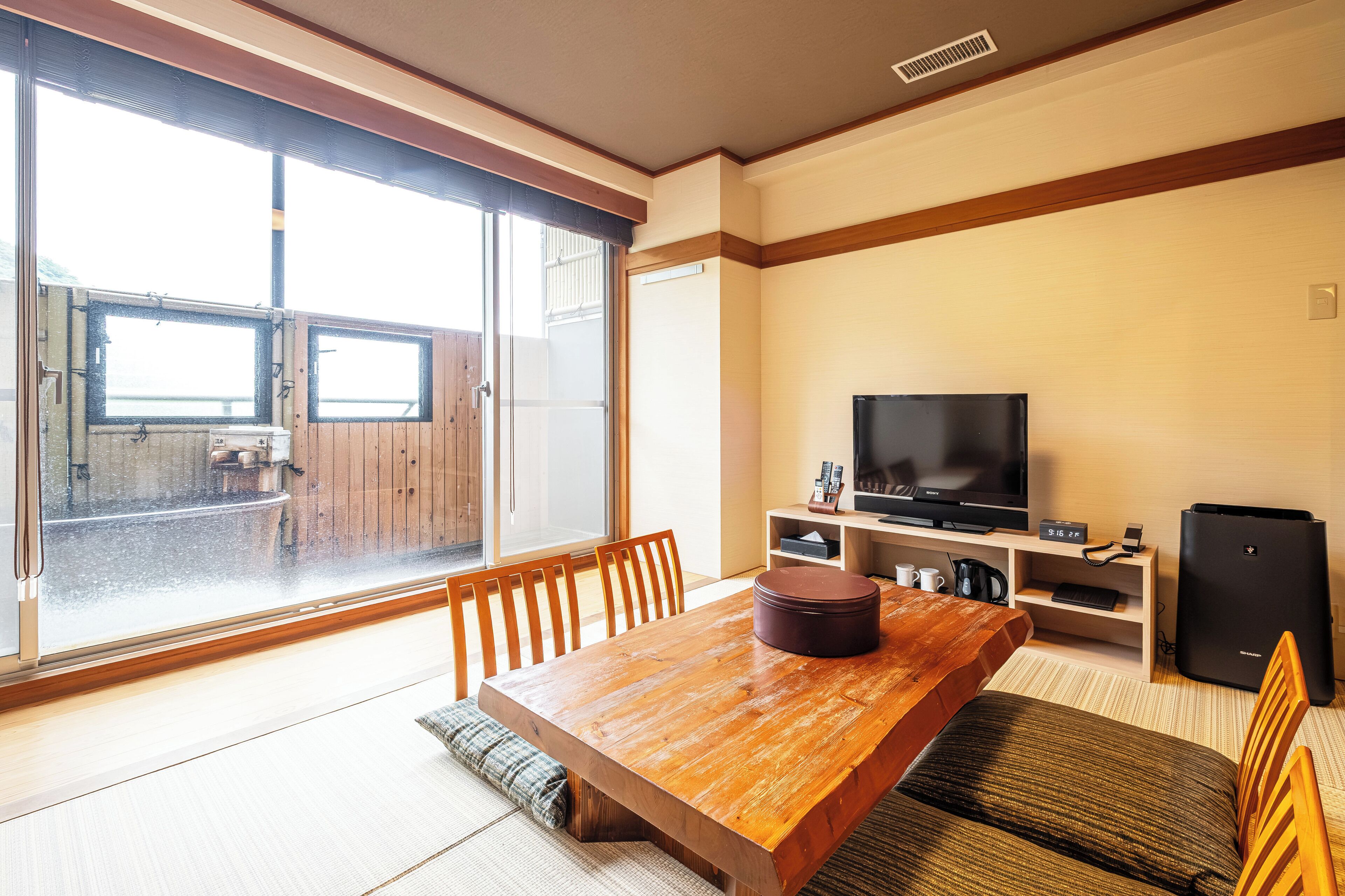 A room with a wooden dining table, chairs, a television, and a refrigerator.