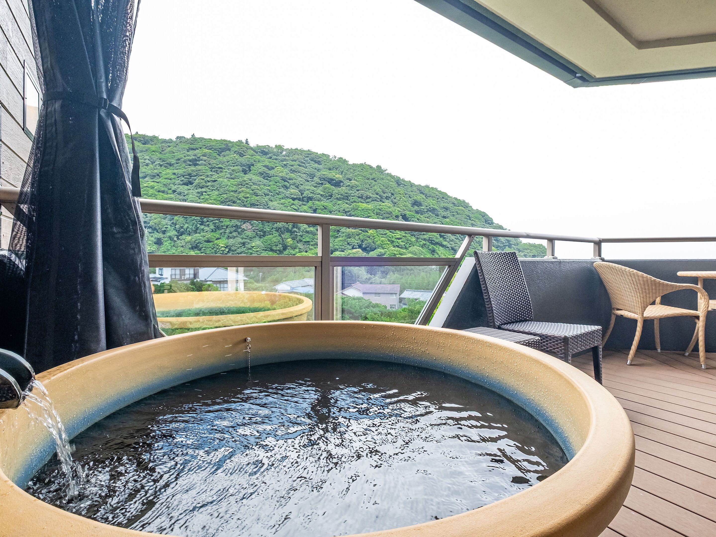 A hot tub on a balcony with a view of a green hill.