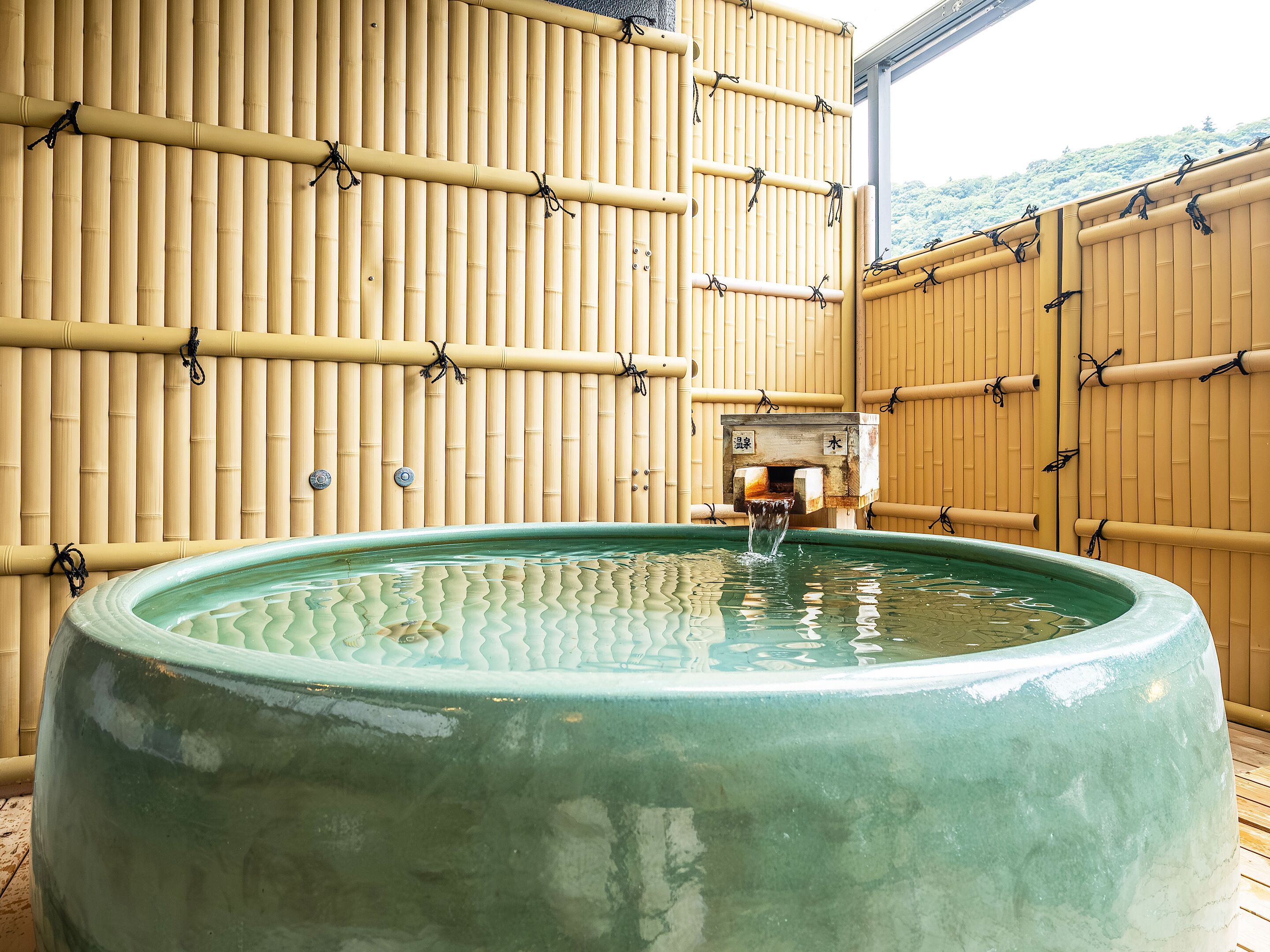 Un jacuzzi grande de color verde con paredes de bambú y piso de madera.