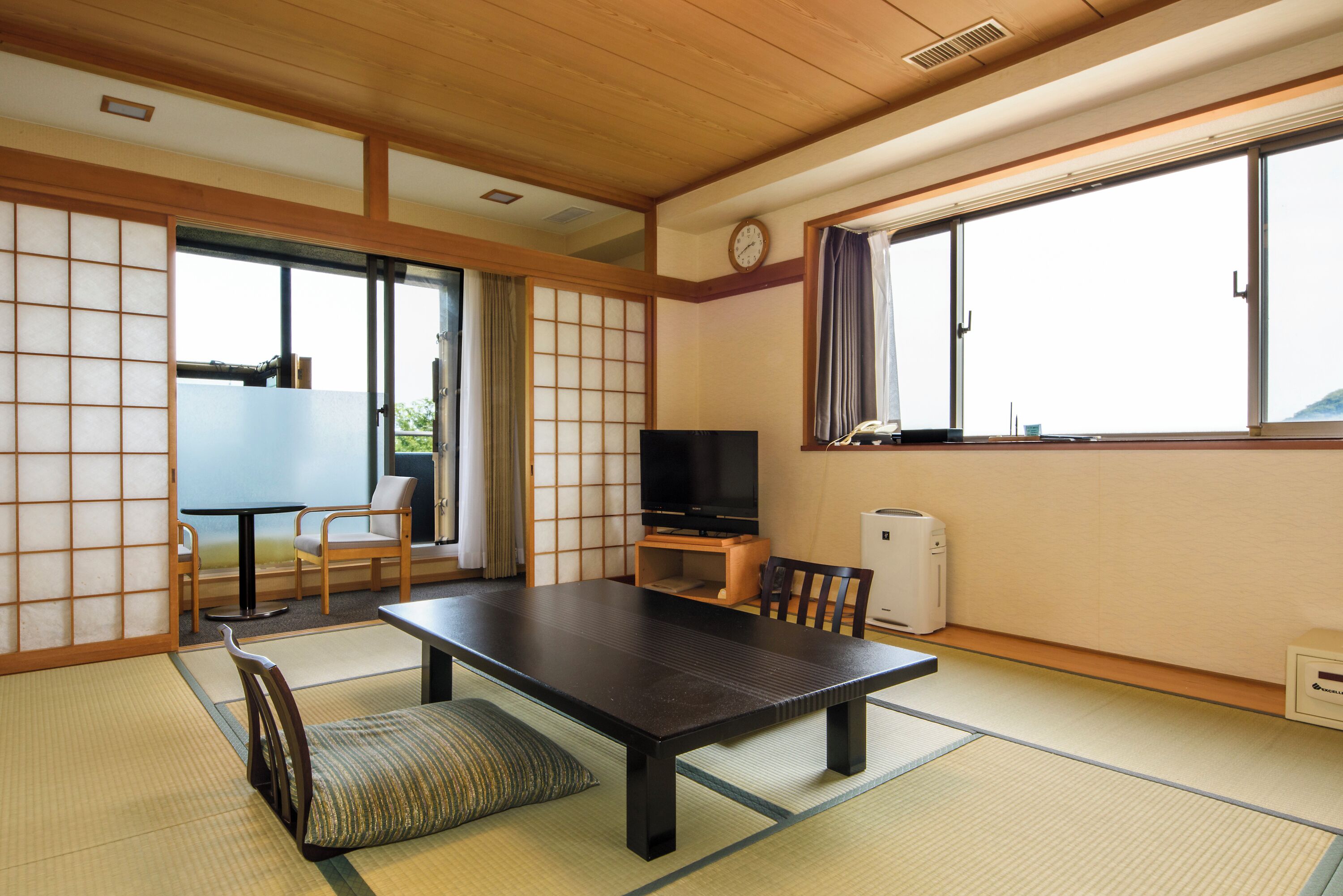 Una habitación japonesa tradicional con suelo de tatami, una mesa baja, sillas, un televisor y una puerta corredera.