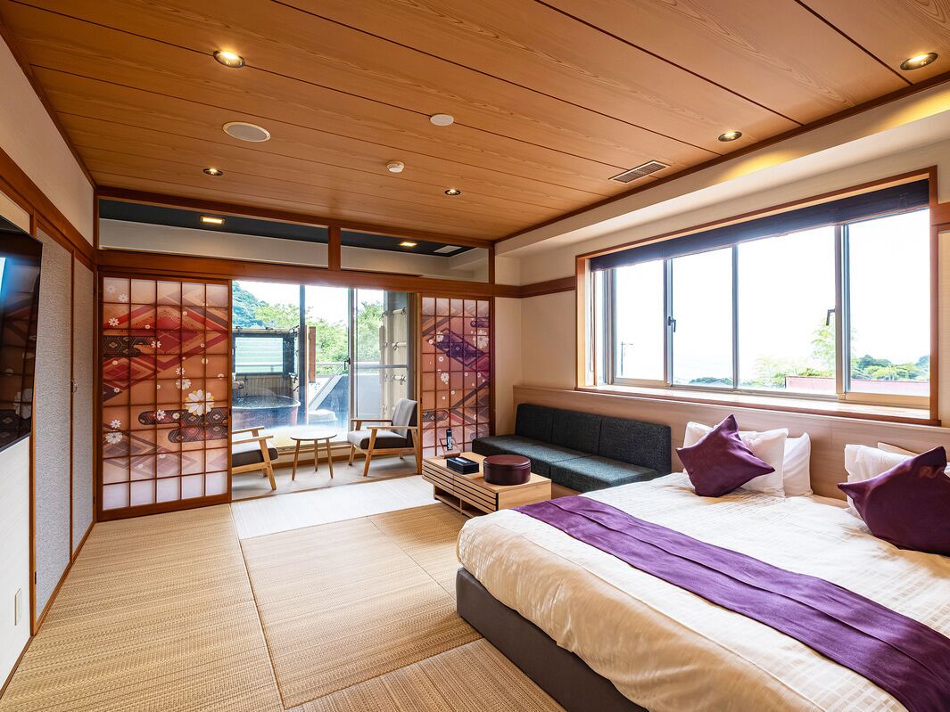 Una habitación de hotel moderna con una cama grande, zona de estar y vistas al exterior.
