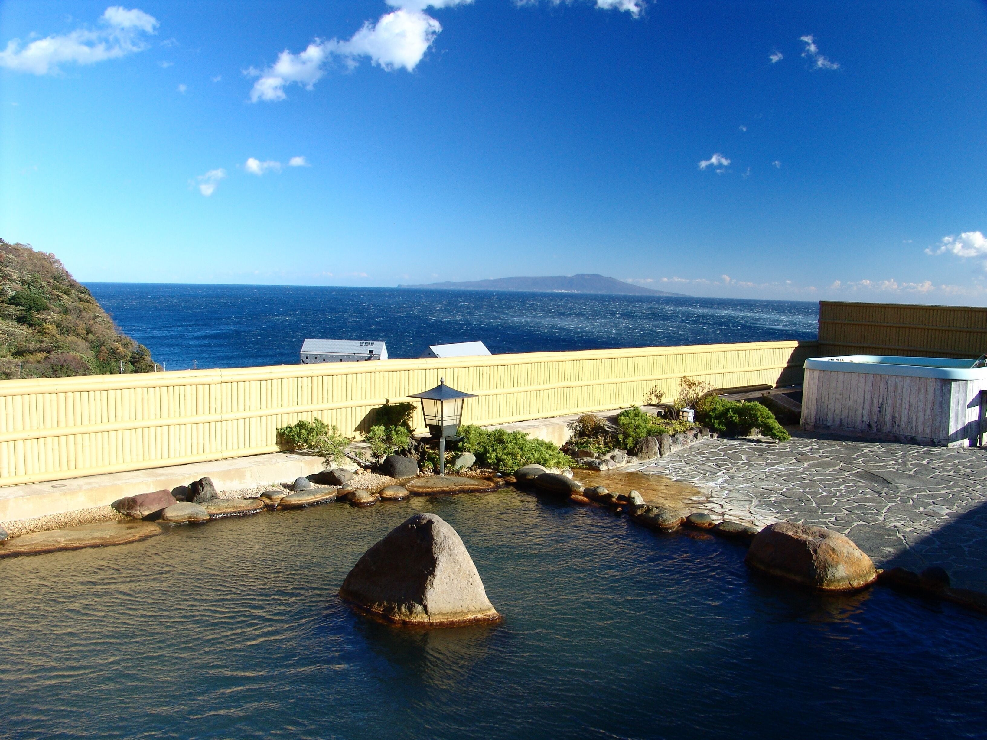 A coastal view with a yellow railing, a stone pathway, and a small water feature with rocks.