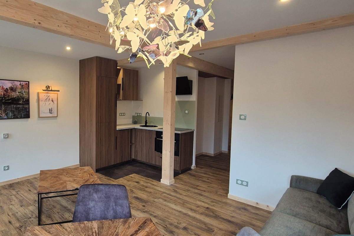 A modern living room with a wooden floor, a dining table, a sofa, and a kitchen in the background.