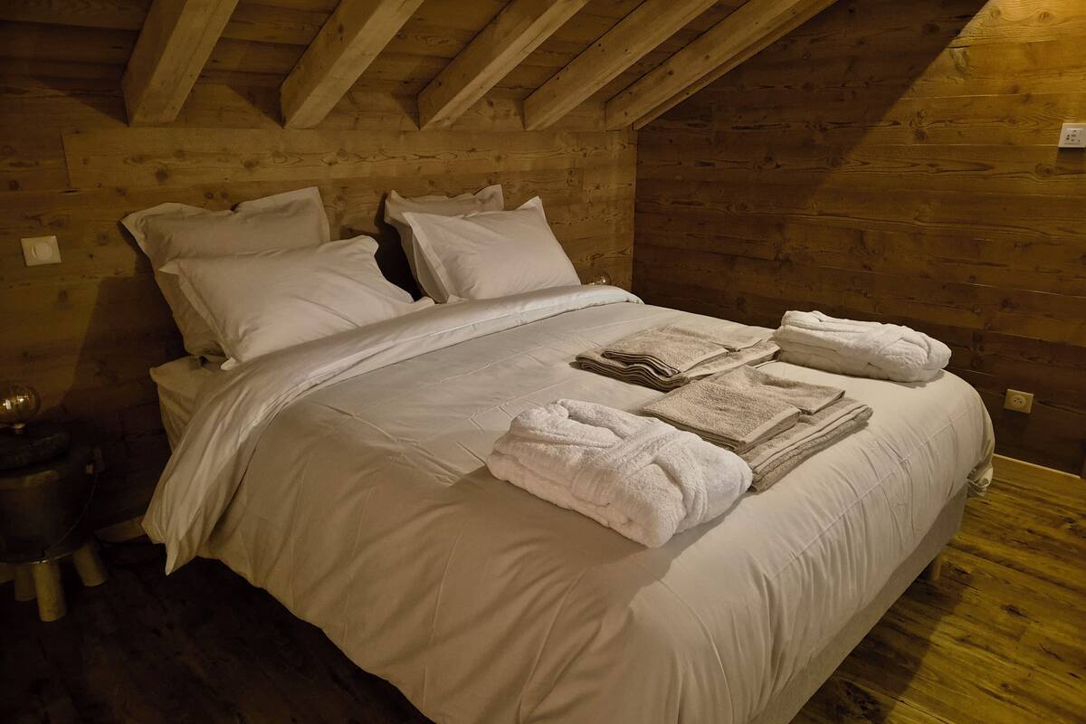 A wooden-paneled room with a bed, pillows, and neatly folded towels.