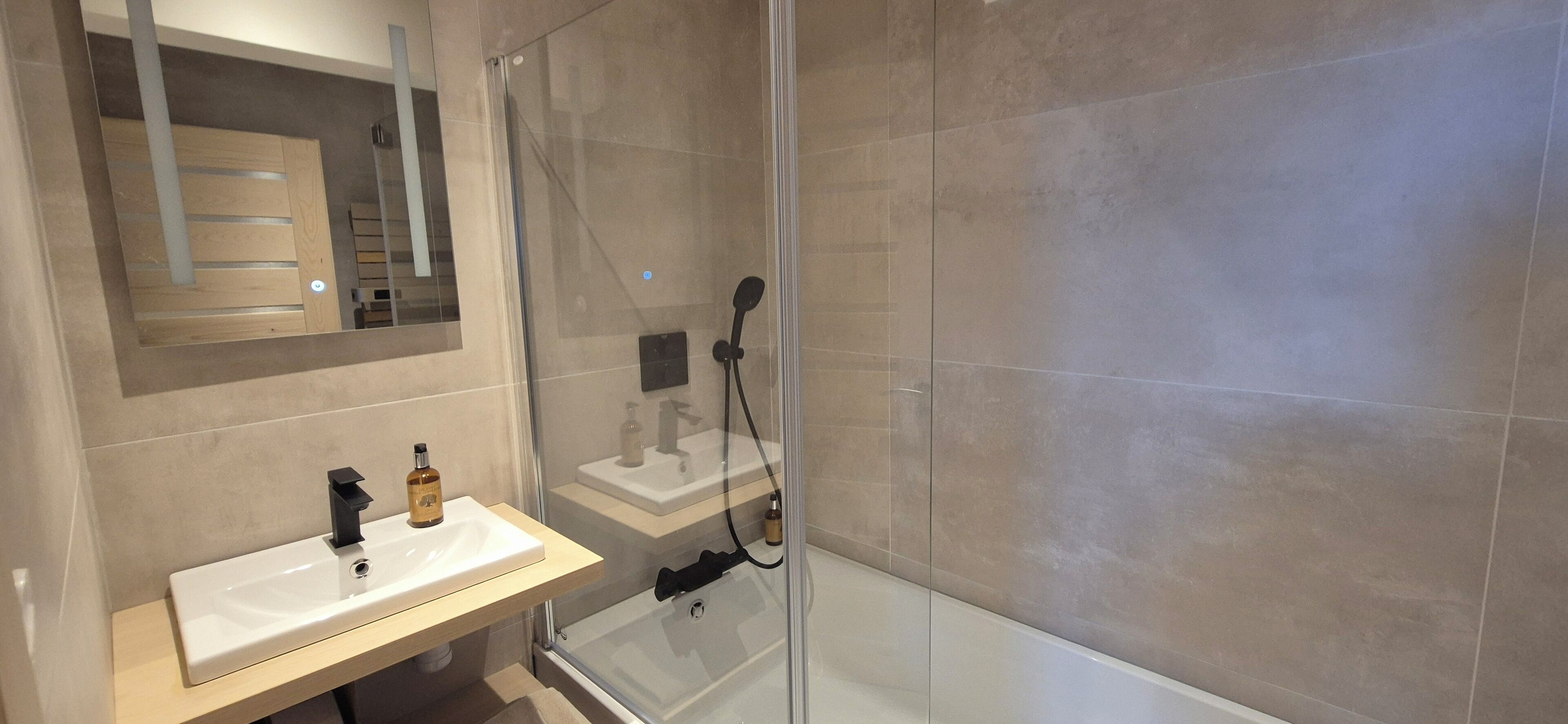 Un baño moderno con ducha envuelta en vidrio, lavamanos blanco y tocador de madera.