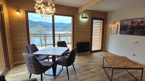 Un espace repas avec une grande table et des chaises, des murs en bois, une vue sur un lac et des montagnes, et des œuvres d’art accrochées aux murs.