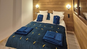 Une chambre avec un plafond en bois, un lit avec une literie bleue et deux lampes fixées au mur.