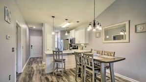 A modern kitchen with a central island, pendant lighting, and a dining area with a table and chairs. - Good Vibes on the Green | Bright, Airy 2BR River Oaks Stay (Myrtle Beach)