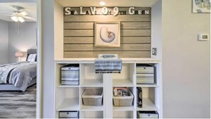 A bedroom with a bed, a ceiling fan, and a wall-mounted shelf with storage bins and a framed picture. - Good Vibes on the Green | Bright, Airy 2BR River Oaks Stay (Myrtle Beach)