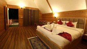 A bedroom with a wooden floor, a bed with white bedding and red pillows, a nightstand, and a small table with chairs. - Niyama Jungle Resort (Sadhupul)