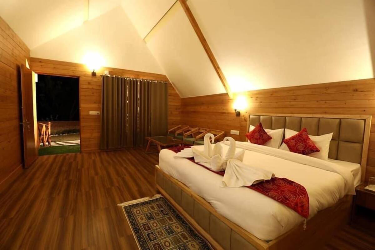 Una camera da letto con pavimento in legno, un letto con biancheria bianca e cuscini rossi, un comodino e un piccolo tavolo con sedie.