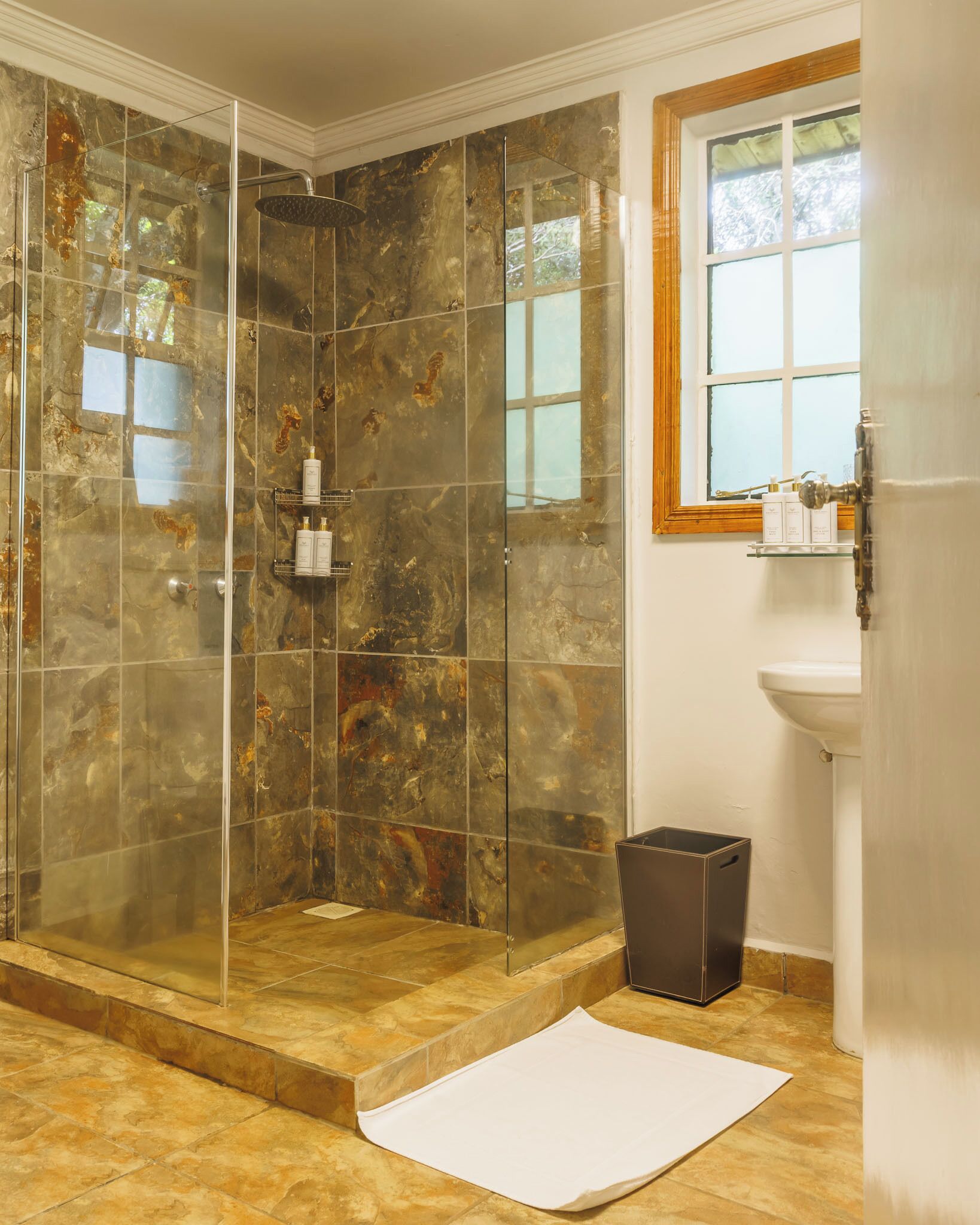 A shower with glass doors, a sink, and a window.