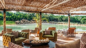 Een overdekt terras met comfortabele banken en fauteuils, een bijzettafeltje met decoratieve eieren, en uitzicht op een kalm meer en groen.