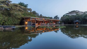 A riverside restaurant with outdoor seating, a dock, and a reflection in the water. - Hemingways Eden Residence (Ongata Rongai)