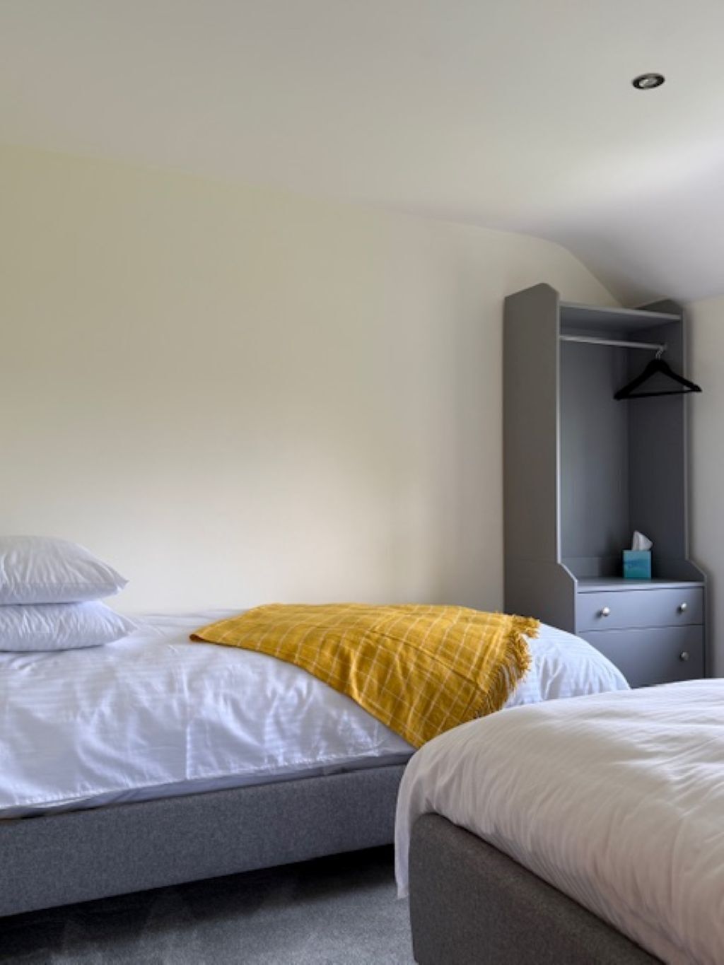 A bedroom with a bed, a bedside table, a hanging coat rack, and a wardrobe.