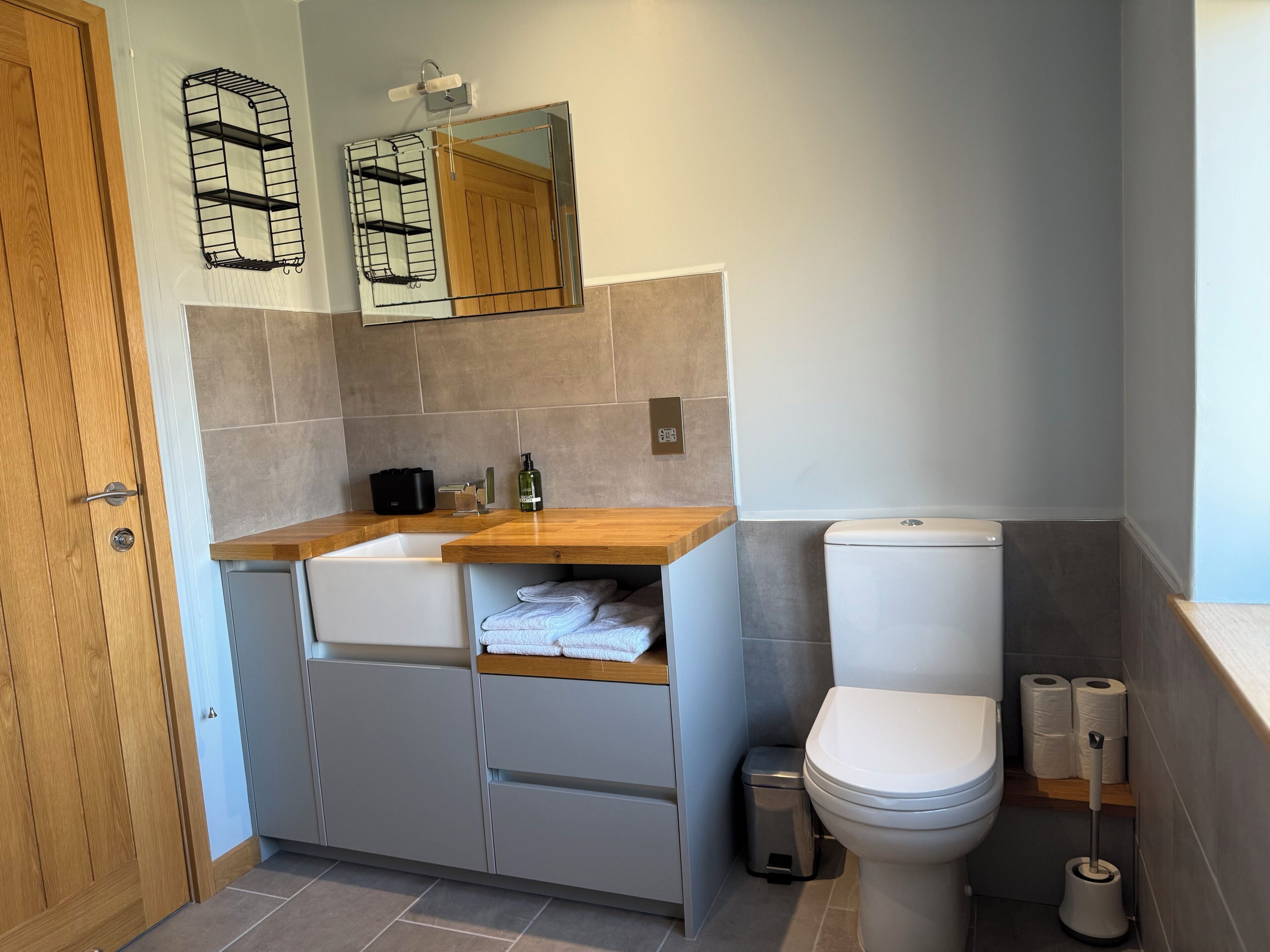 Un baño moderno con tocador de madera, un espejo, inodoro y un cubo de basura.