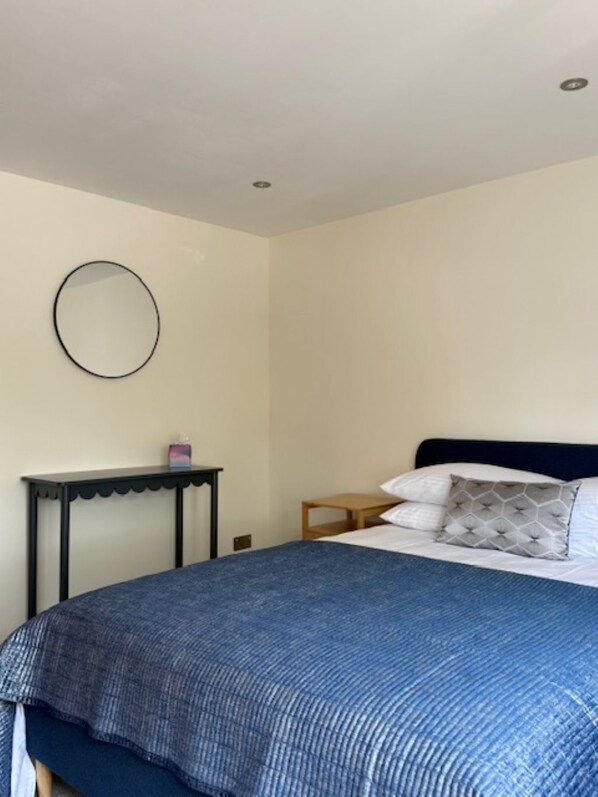 A bedroom with a bed, a round mirror, a small table, and a nightstand. - Family home close to Lulworth Cove, Durdle Door, The Tank Musuem & Monkey World (Wool)