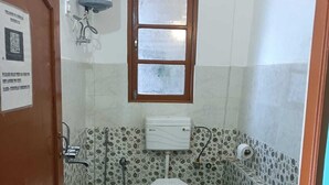 Ένα μικρό μπάνιο με τουαλέτα, ντους και νιπτήρα. Υπάρχει ένα παράθυρο πάνω από την τουαλέτα και μια πόρτα στα αριστερά.