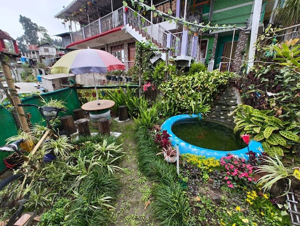 A lush garden with a small pond, various plants, and a bicycle. - Kusuman Homestay (Kalimpong)