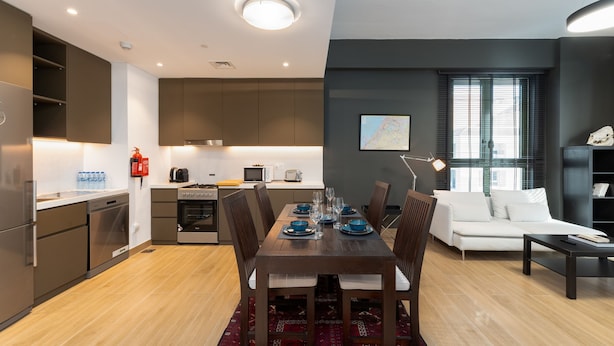 Eine moderne Küche mit Einbaugeräten, ein Essbereich mit Holztisch und -stühlen sowie ein Wohnbereich mit Sofa und Couchtisch.