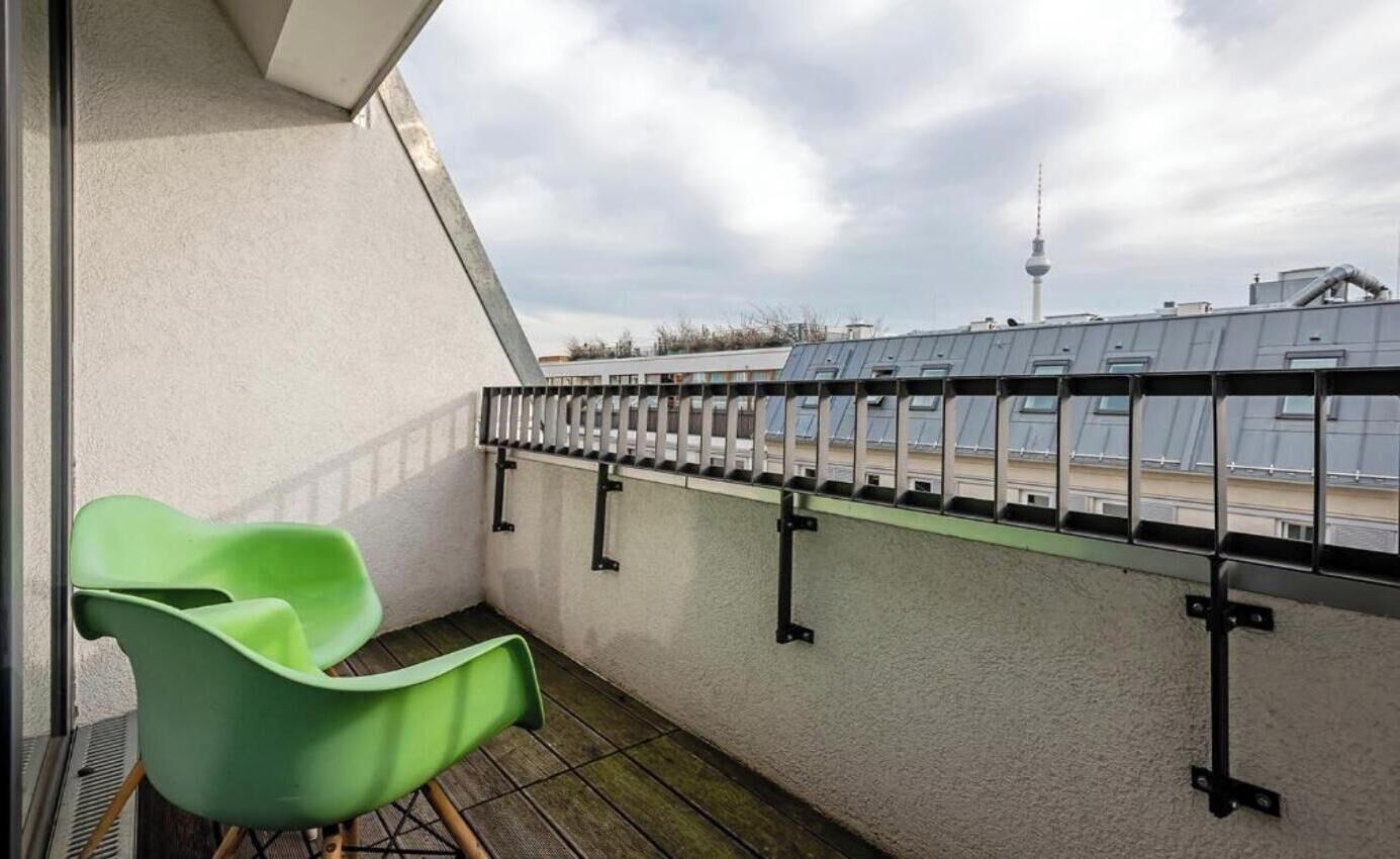 A balcony with a green chair, a metal railing, and a view of a tower in the background.