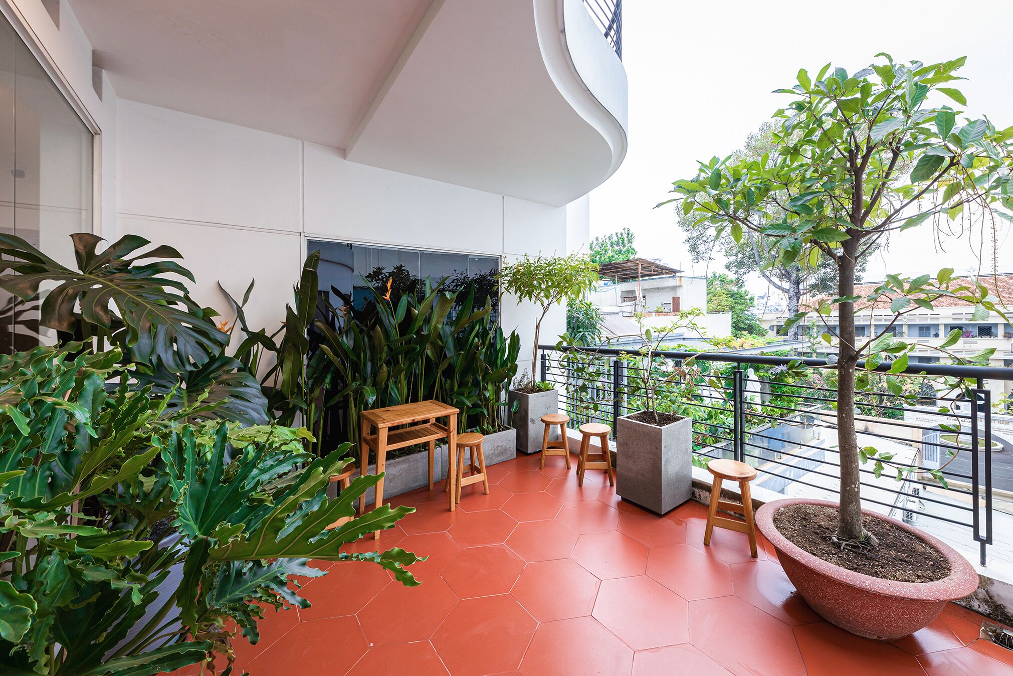 Un balcón con mesa y sillas de madera, rodeado de plantas en macetas y una jardinera grande con un árbol.