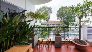 A balcony with a wooden table and stools, surrounded by potted plants and a large planter. - Lynn by La Doma Express (Ho Chi Minh City)