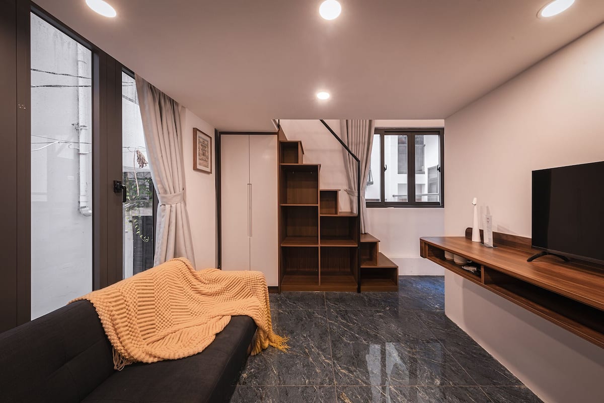 A modern living room with a sofa, a TV, and a staircase leading to a loft area.