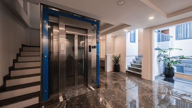 A modern lobby with a marble floor, a blue elevator, and a staircase leading to an upper level. - Lynn by La Doma Express (Ho Chi Minh City)