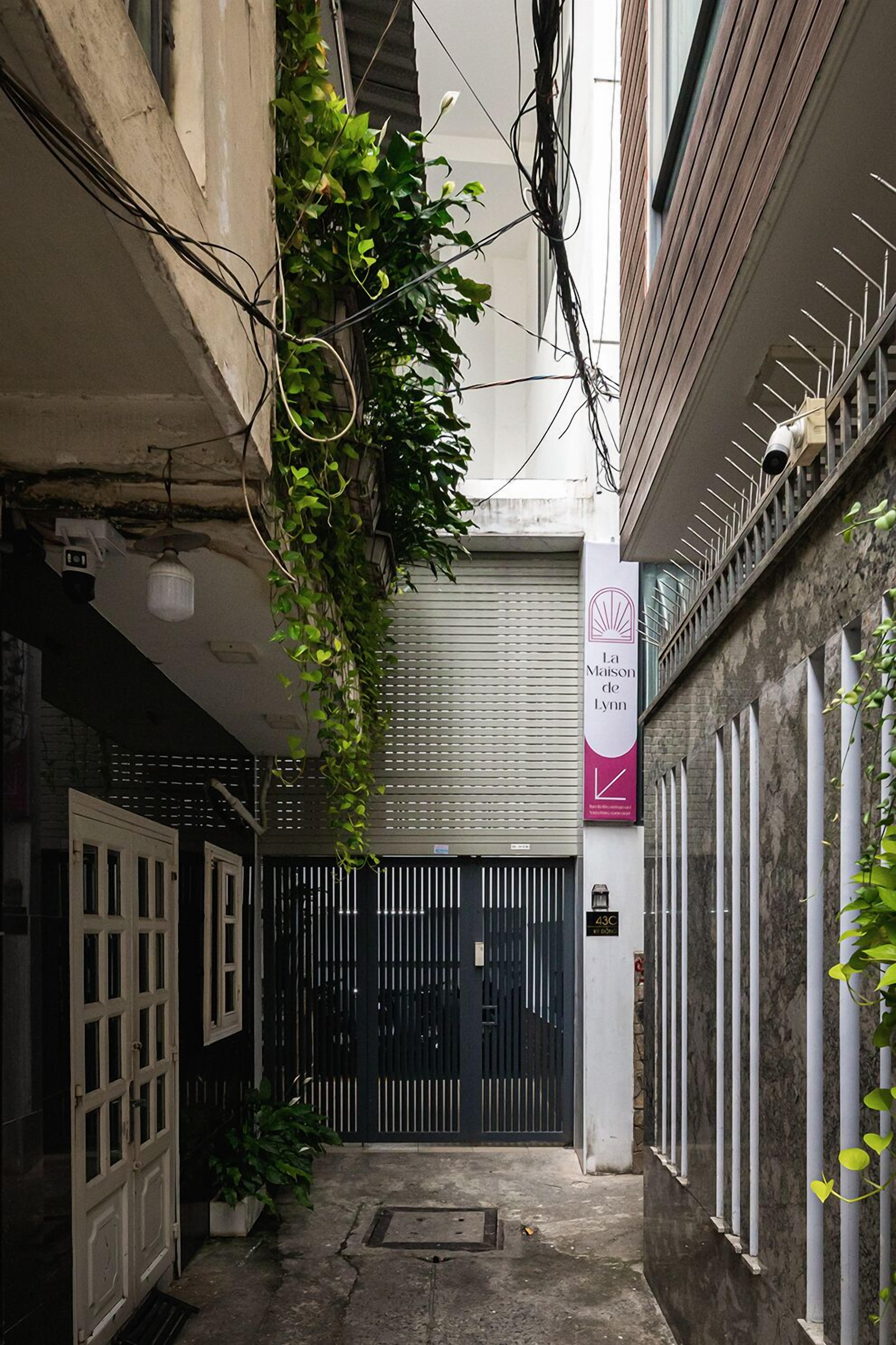A narrow alleyway with a black gate, a white door, and a sign for "La Maison de Lyon".