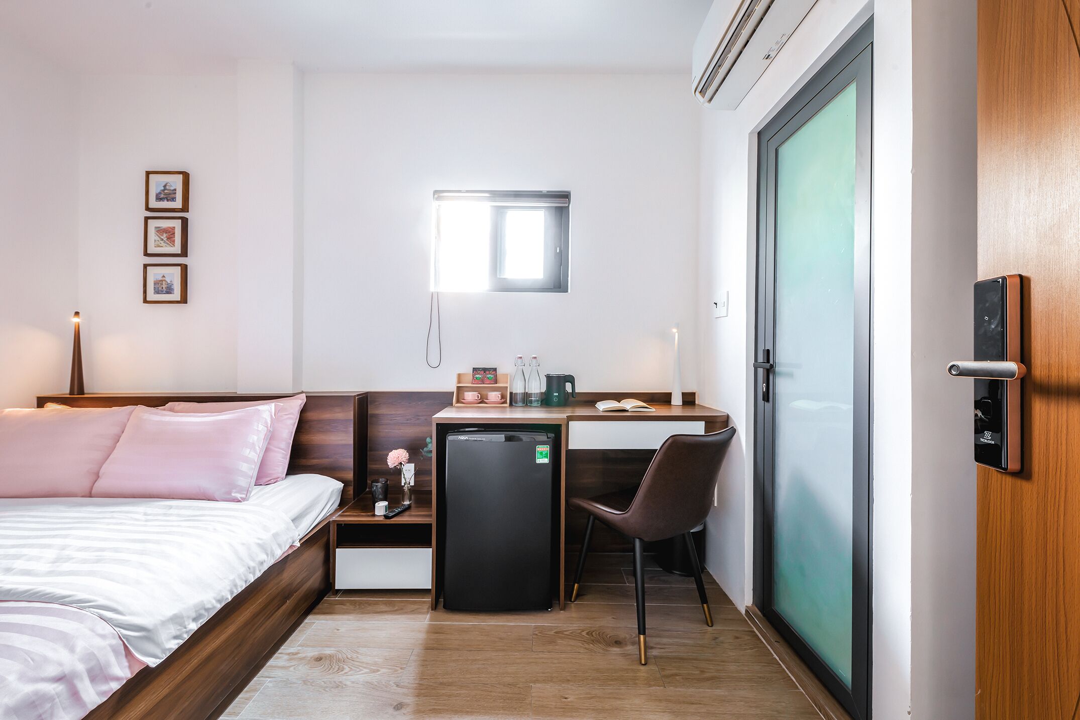 Habitación de hotel pequeña y funcional, con cama, escritorio, silla, refrigerador y puerta corrediza.