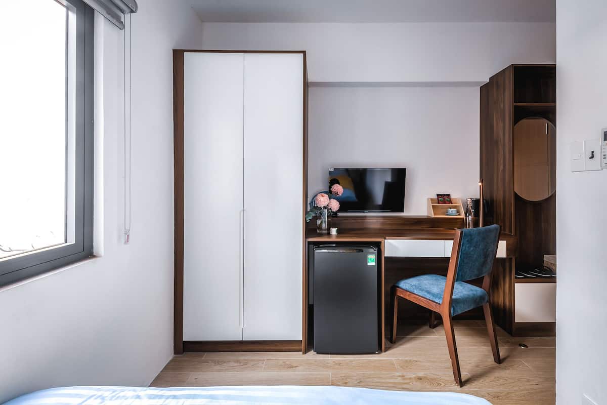 A compact hotel room with a bed, a desk with a computer, a small fridge, a TV, and a wardrobe.