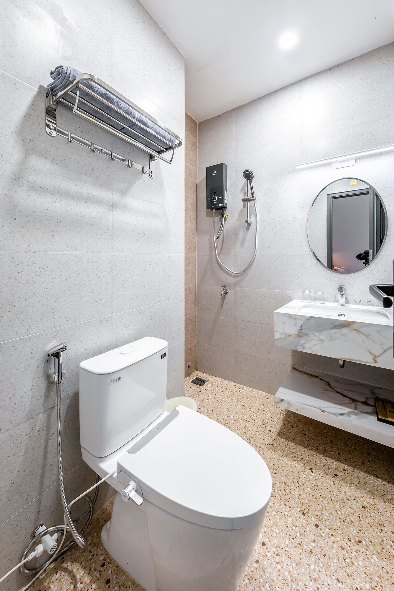 A modern bathroom with a toilet, a shower unit, a sink with a marble countertop, and a towel rack.