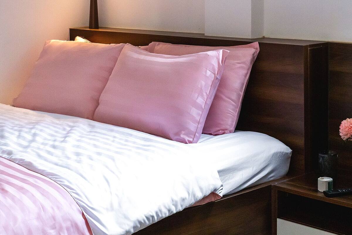 A neatly made bed with pink and white linens, a bedside table with a remote control, and three framed pictures on the wall.
