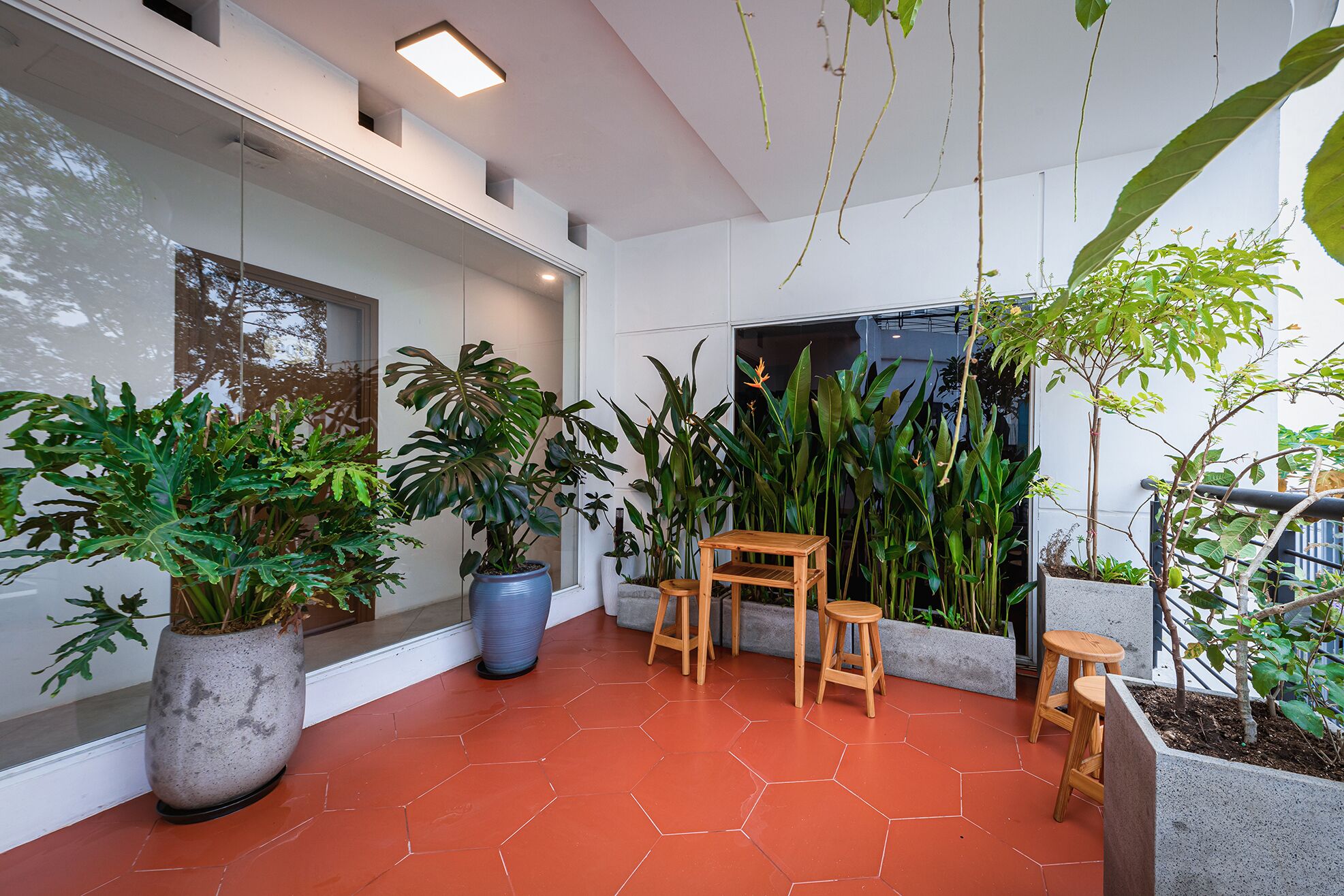 A modern indoor space with hexagonal red tiles, potted plants, and wooden furniture.