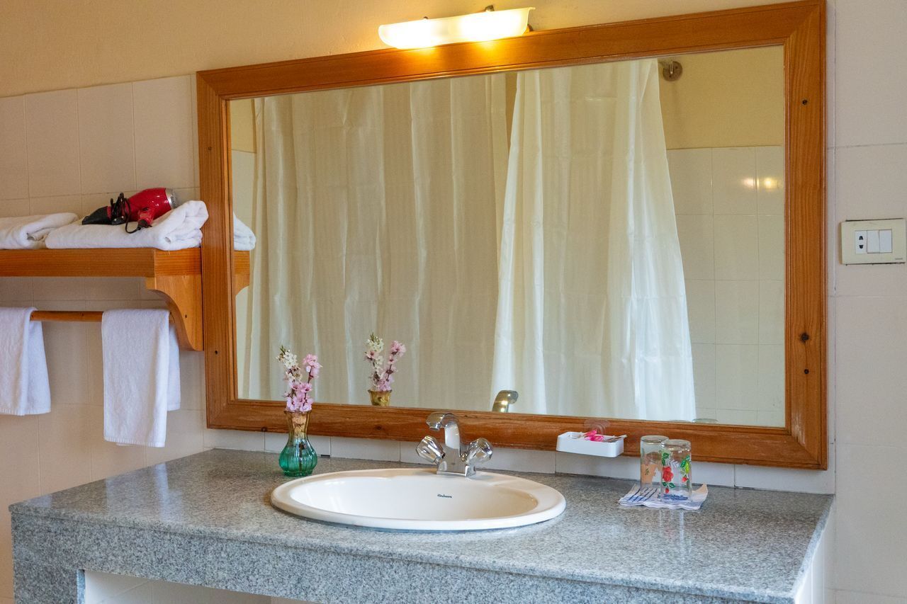 Un baño con un espejo grande, un lavamanos y un perchero para toallas.