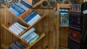 A room with wooden bookshelves filled with books, a patterned wall, and a woven blanket. - Hotel Jakar View (Bumthang)