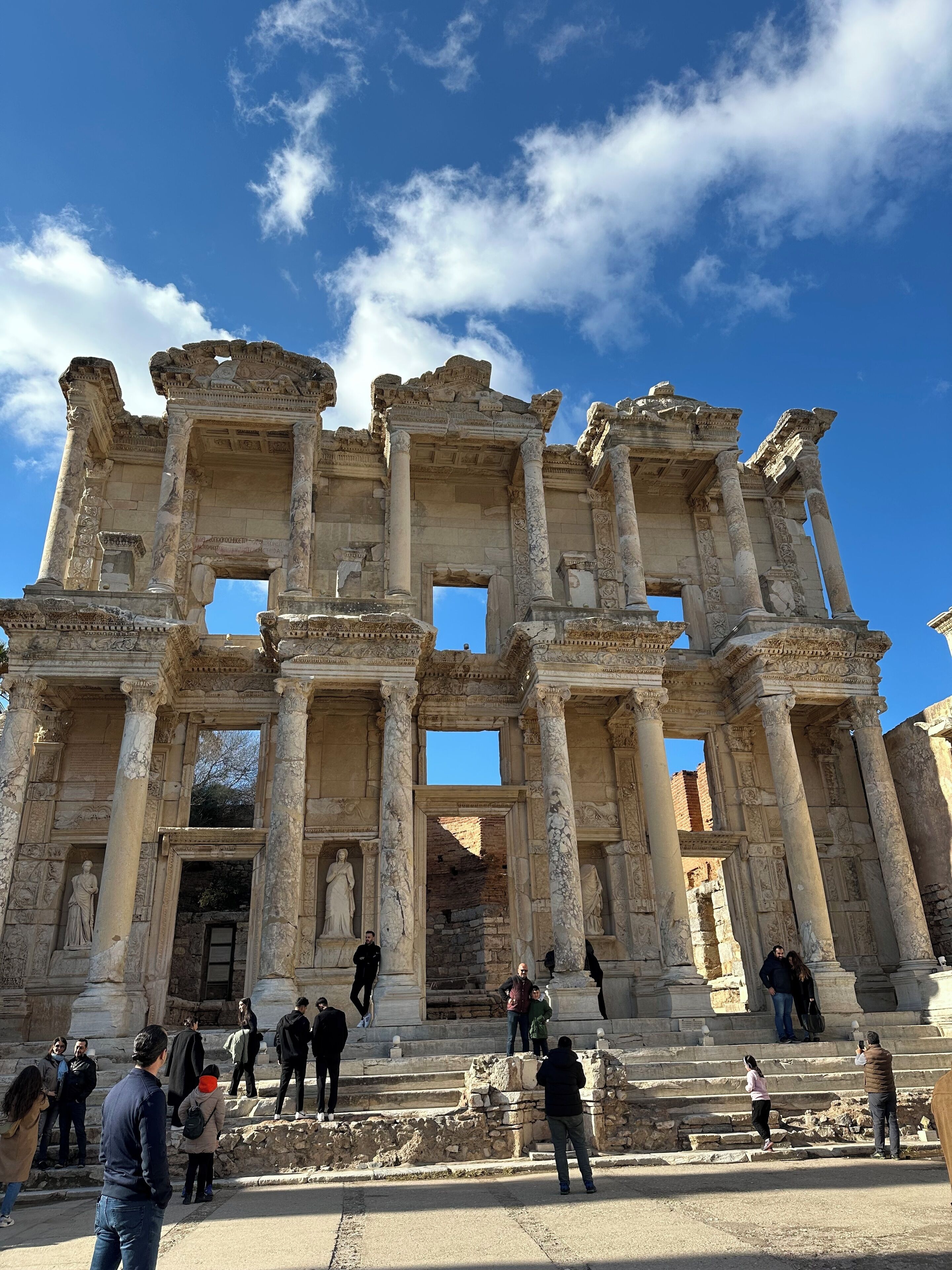 An ancient ruin with columns and statues, surrounded by visitors.