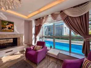 Una sala de estar con chimenea, vista a la piscina y mobiliario púrpura.