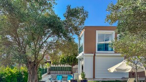 A residential property with a swimming pool, outdoor seating, and a large tree.