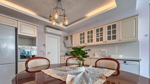 A modern kitchen with white cabinets, a stainless steel refrigerator, a Bosch dishwasher, and a dining table with two chairs.