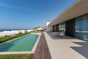A modern outdoor pool area with a clear view of the ocean, a wooden deck, and a seating area with a table and chairs. - Al Zorah Villa - Mint Stay (Ajman)