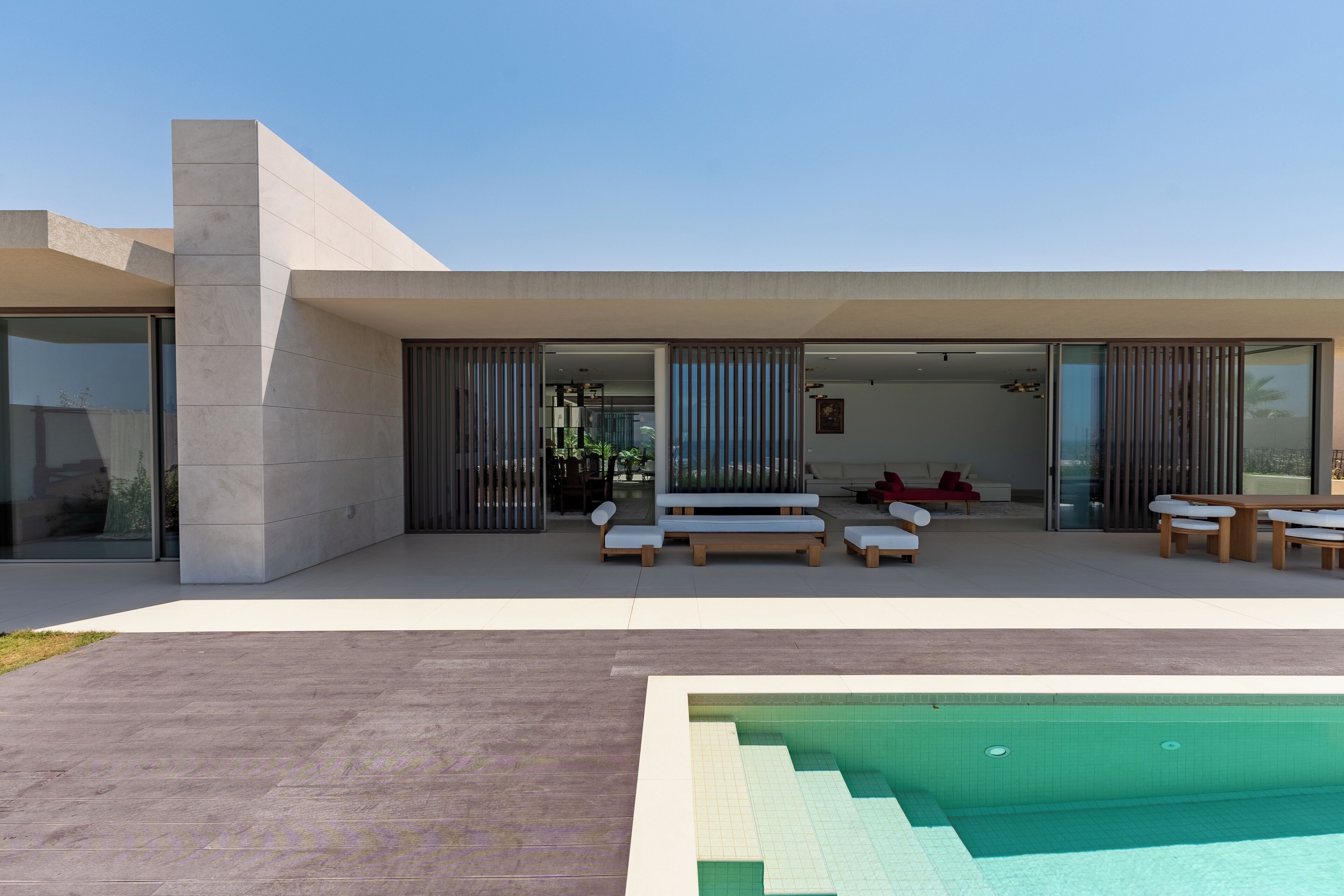 Et moderne udendørs poolområde med minimalistisk design, der inkluderer en pool, siddepladser og en klar himmel.