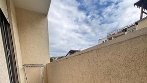 A balcony with a metal chair, beige walls, and a view of the sky and neighboring buildings. - Sea Front Apartment - Tranquil Retreat in Albania (Rrashbull)