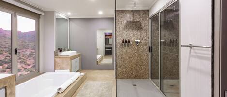 A modern bathroom with a large bathtub, a walk-in shower, and a view of the desert landscape.