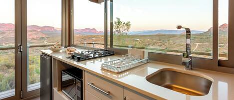 A modern kitchen with a large window offering a scenic view of a desert landscape.