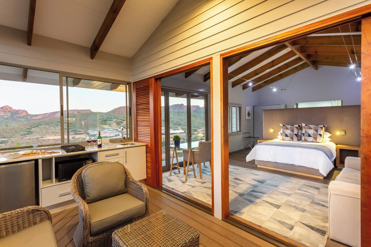 A bedroom with a large bed, a desk with a computer, and a view of the desert through large sliding glass doors.