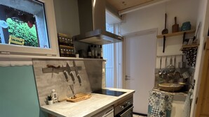 Eine kompakte Küche mit integriertem Geschirrspüler, Backofen und einer kleinen Kochinsel mit Spüle. Über der Spüle befindet sich ein Fenster, die Decke ist aus Holz und der Boden ist mit Fliesen belegt.
