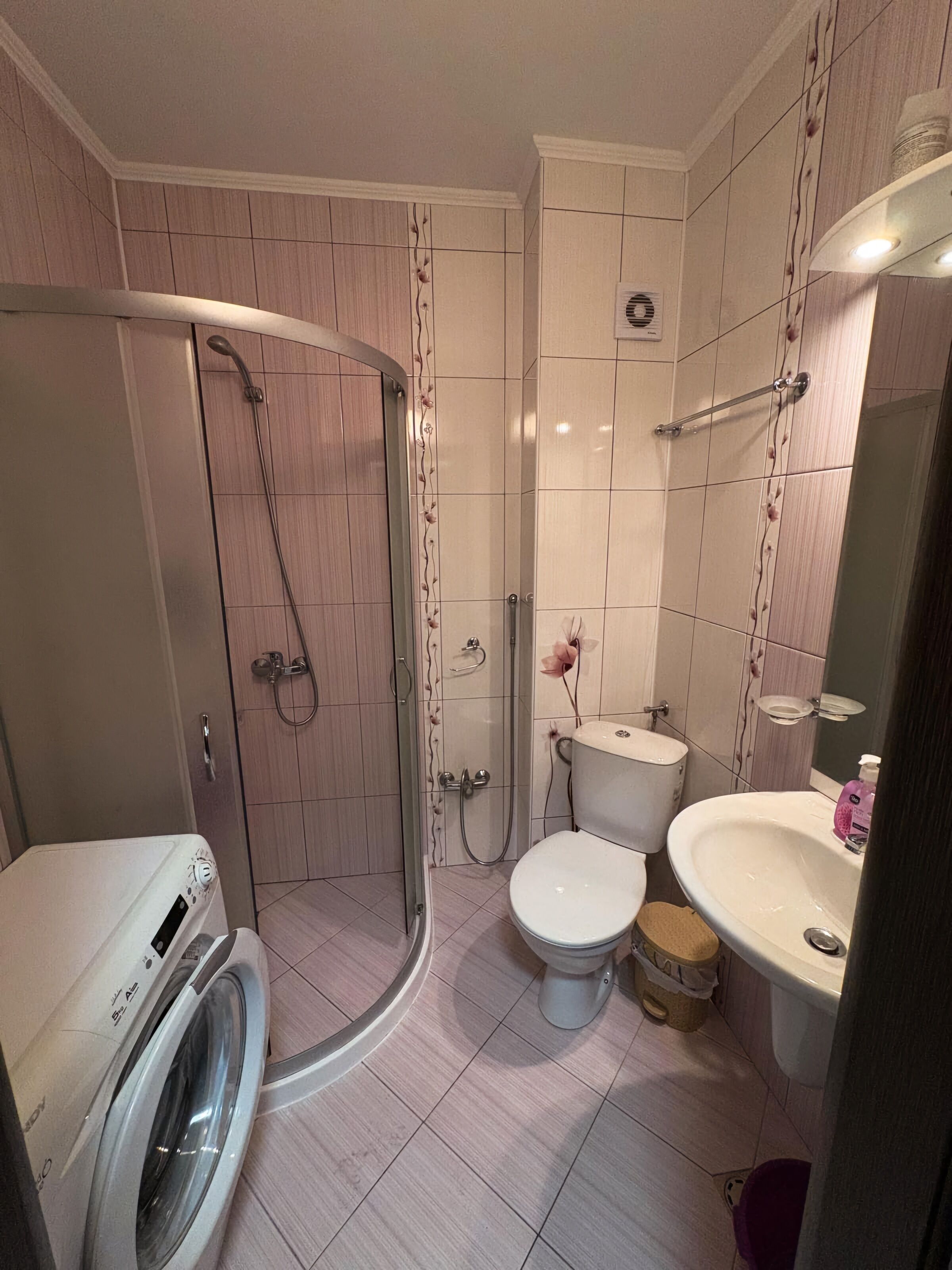 Une salle de bain compacte comprenant un espace douche, des toilettes, un lavabo et un lave-linge.