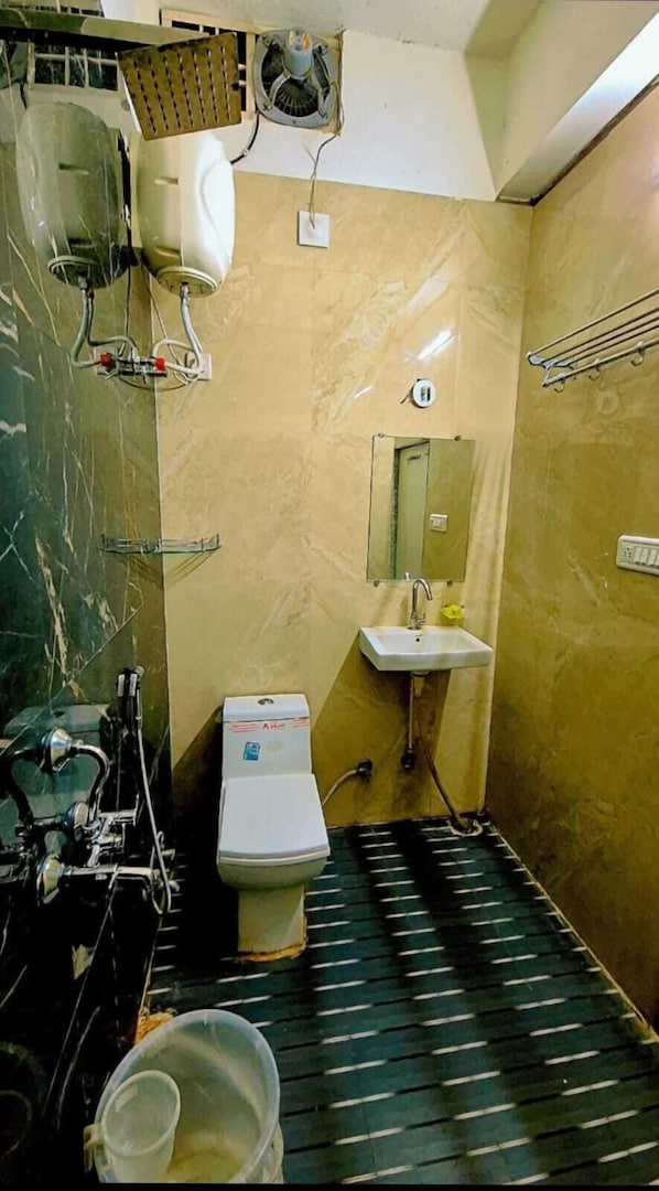 A small bathroom with a toilet, sink, and a mirror. There are pipes and a fan on the wall. - Aangan Palace (Udaipur)